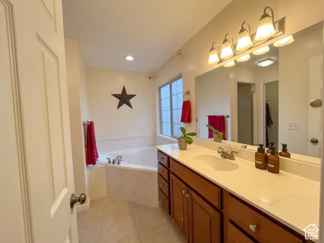 Built-in corner bathtub, vanity with dual sinks, wood-finish cabinetry, ceramic tile flooring, and a large wall-mounted mirror