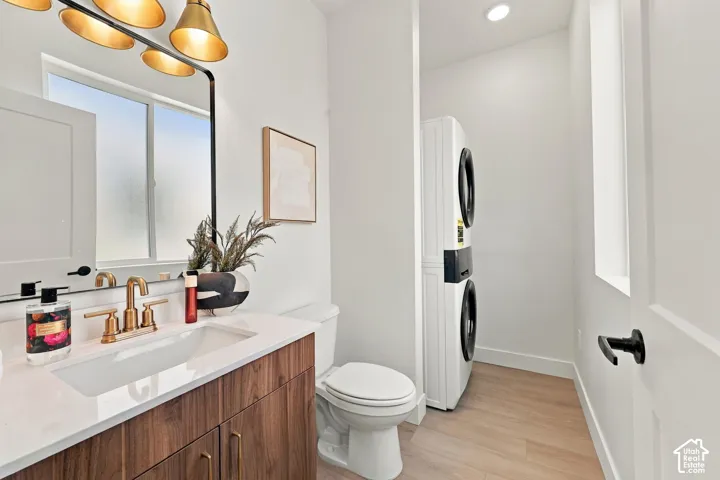 Integrated laundry area with stacked appliances, white quartz vanity, wood-finish cabinetry, and gold-finish hardware