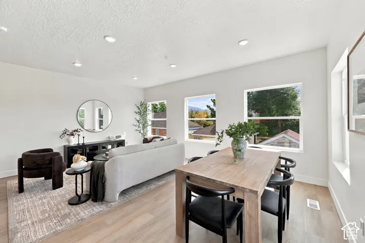 Open-concept living and dining area with wood-finish flooring, recessed lighting, white walls, and multiple windows