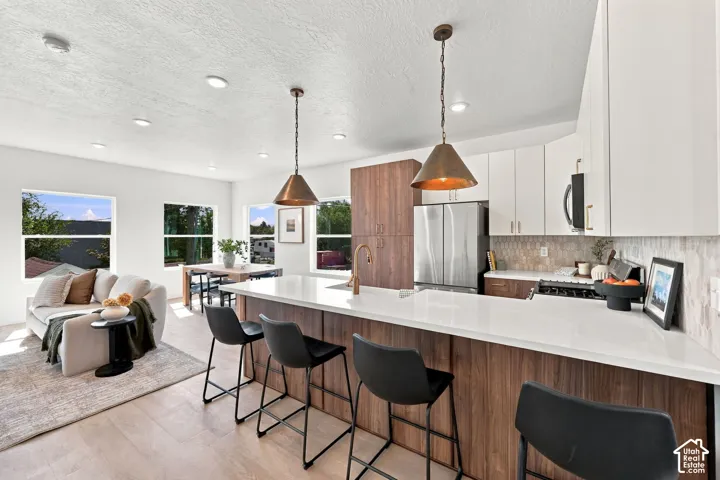 Open-concept living space featuring wood-finish flooring, recessed lighting, a kitchen island with seating, a stainless steel refrigerator, and a gas range