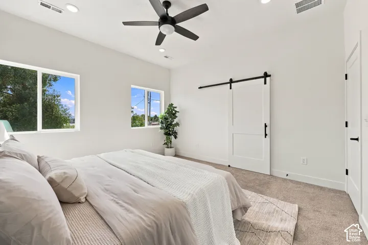 White walls with recessed lighting, ceiling fan, two windows, and a white barn-style door with black hardware
