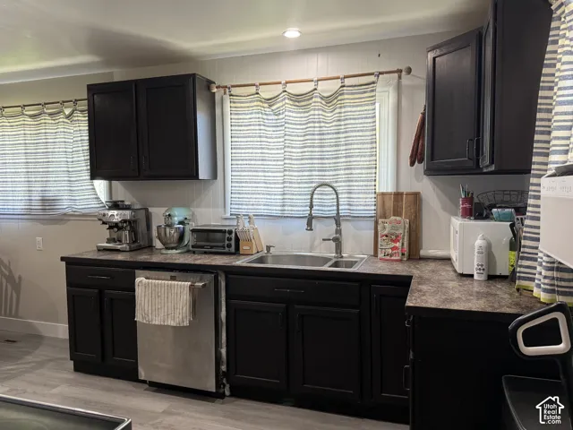 Kitchen featuring dark wood-finish cabinetry, a stainless steel dishwasher, and a double basin sink with a high-arc faucet