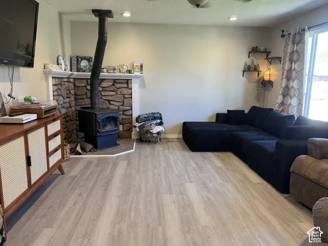 Stone fireplace with a wood-burning stove, light wood-finish flooring, recessed lighting, and a ceiling fan