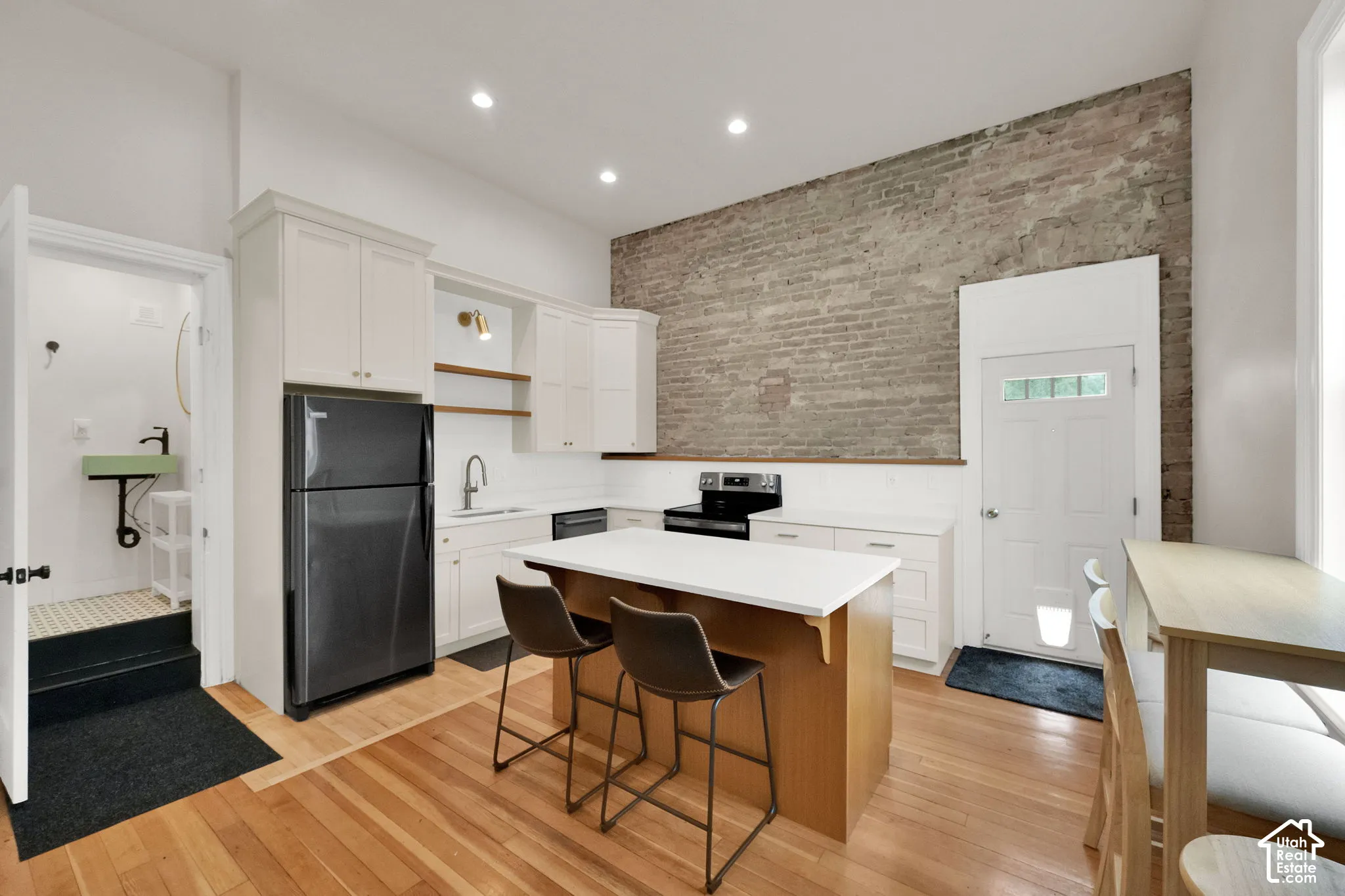 Kitchen featuring wood-finish flooring, white cabinetry, a center island with countertop seating, stainless steel appliances, and an exposed brick accent wall