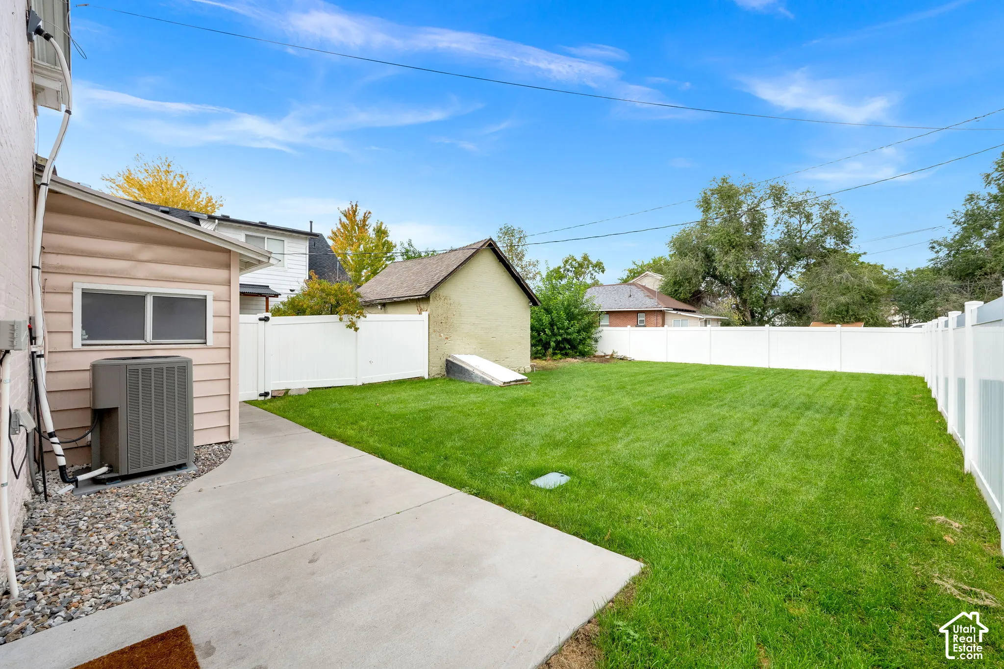 Expansive backyard featuring a manicured lawn, a concrete pathway, a white privacy fence, and a detached shed