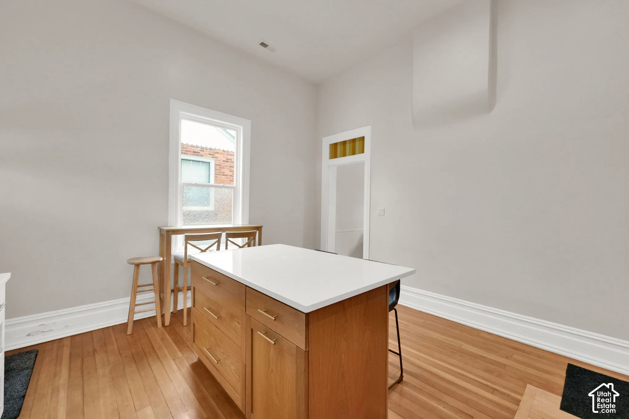 Wood-finish flooring, white trim, recessed lighting, and a kitchen island with a white countertop and natural wood-finish cabinetry