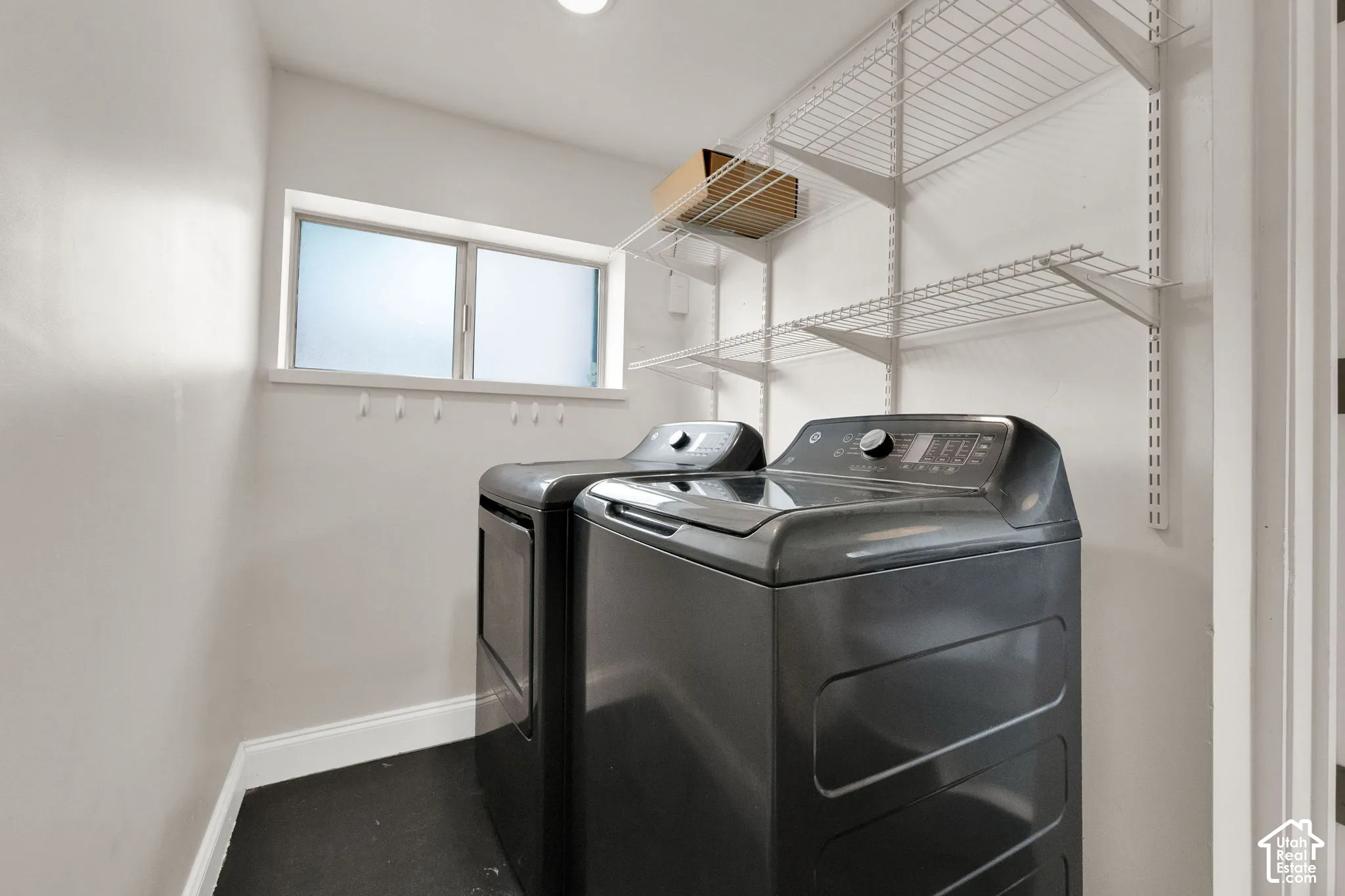 Utility space featuring white walls, wire shelving, a window with frosted glass, and dark flooring