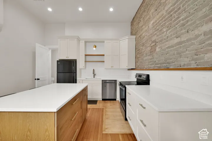 Kitchen featuring an exposed brick accent wall, white cabinetry, a wood-finish island with white countertops, and stainless steel appliances