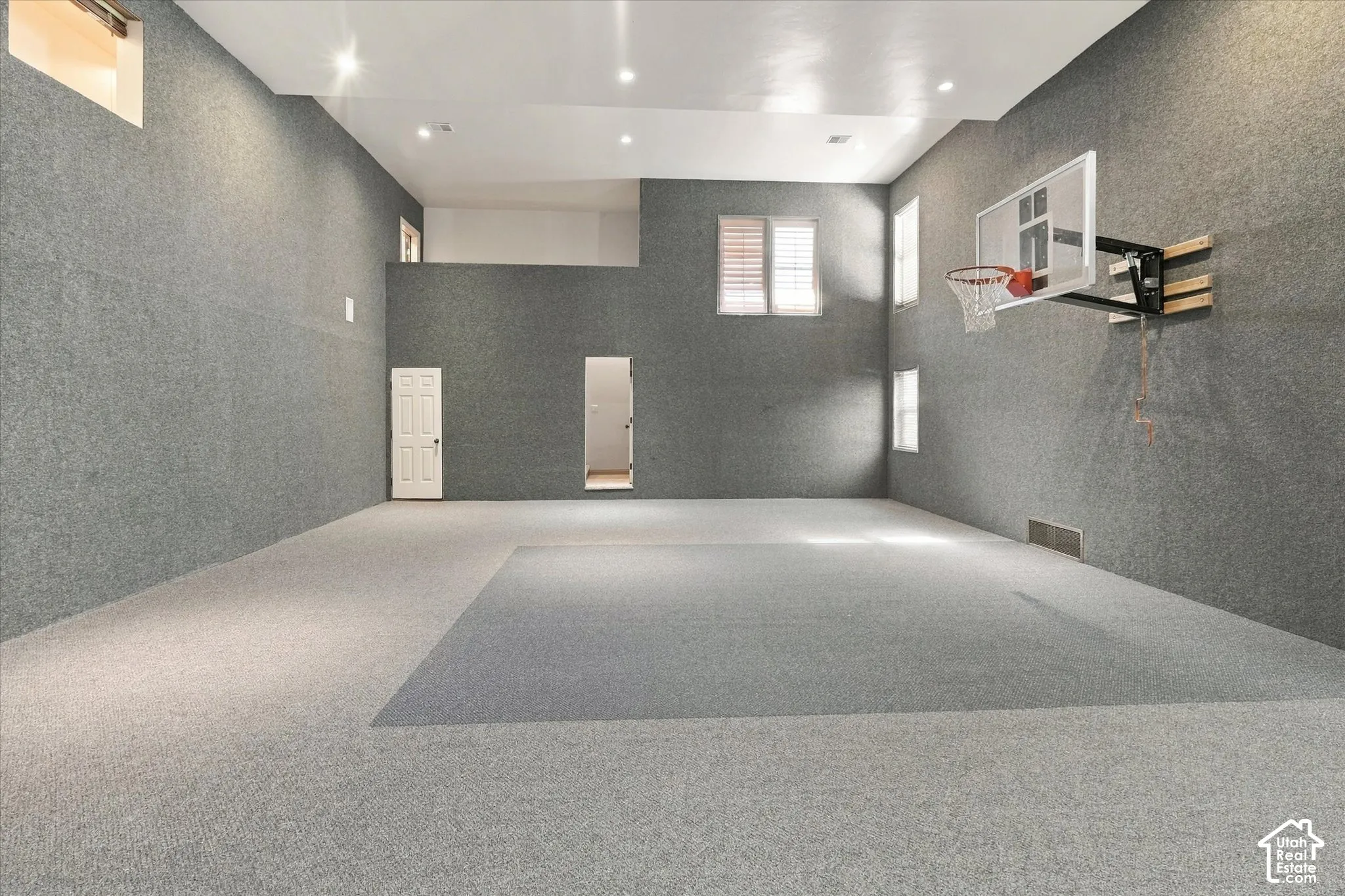 Expansive recreational space featuring two-tone carpeting, high ceilings with recessed lighting, and a mounted basketball hoop