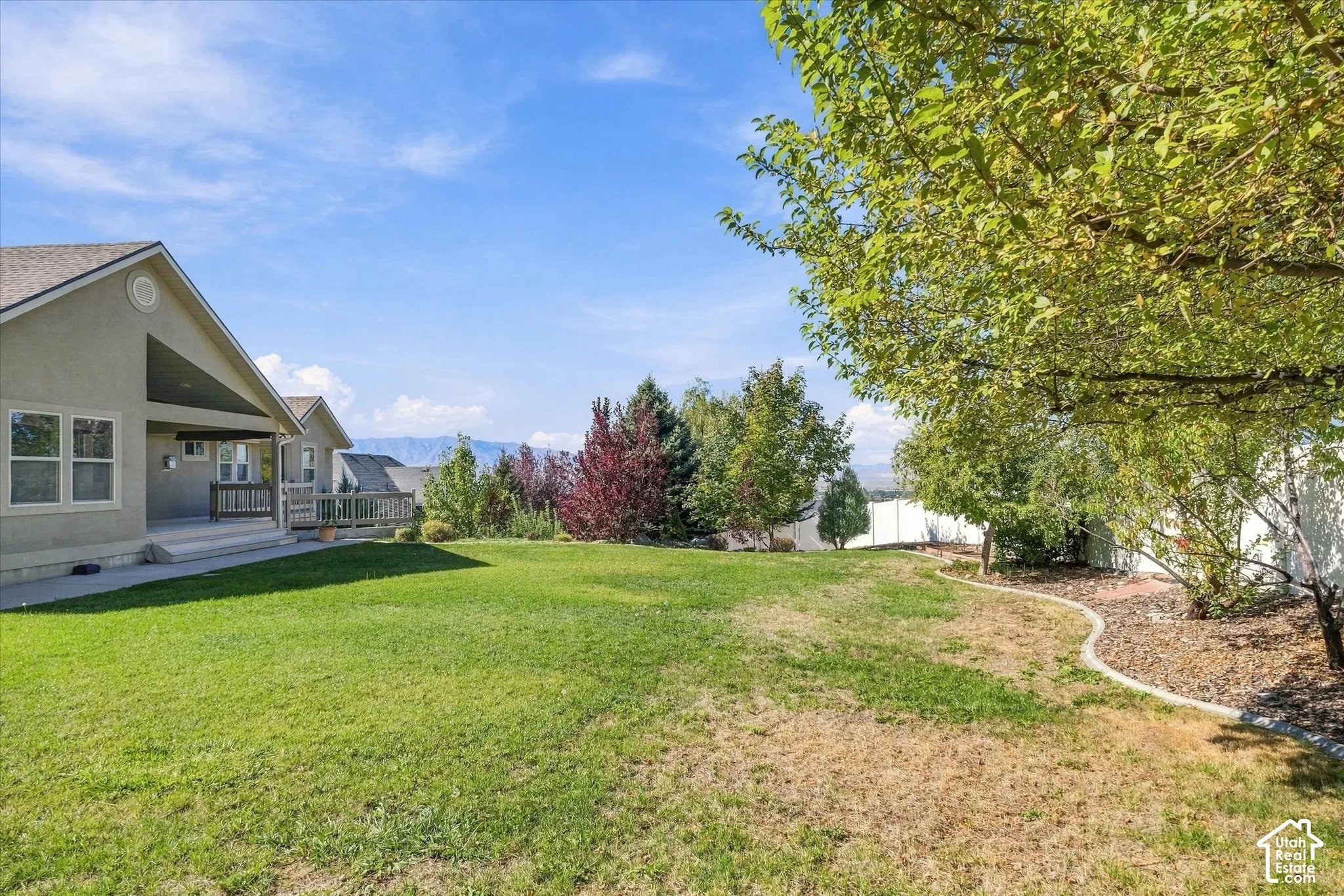 Expansive lawn area with a covered patio, wooden deck, and mature landscaping