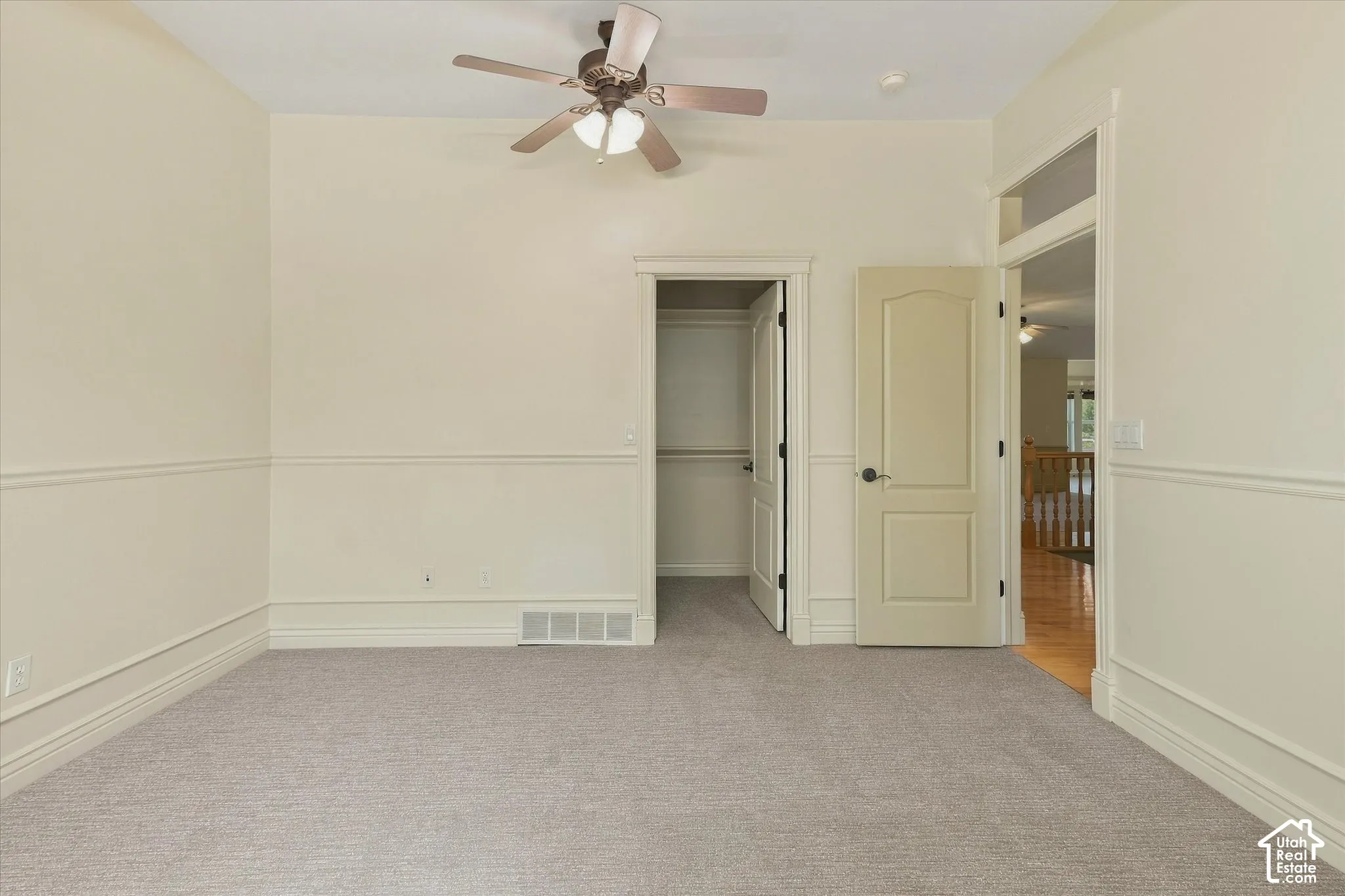 Neutral wall paint, wainscoting detail, ceiling fan with light fixture, paneled doors, and carpeted flooring