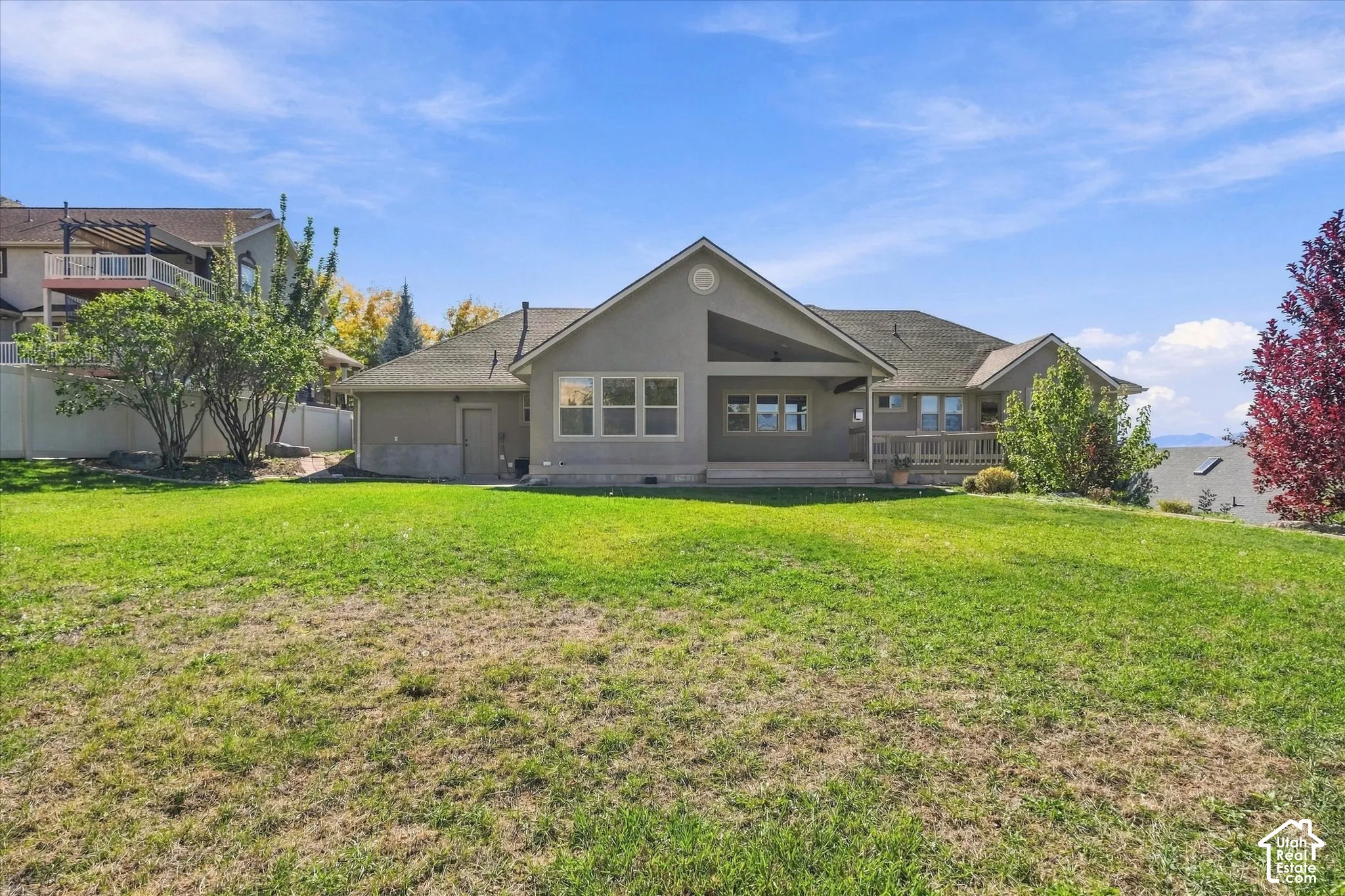 Expansive backyard featuring a manicured lawn, a covered patio, and a wooden deck