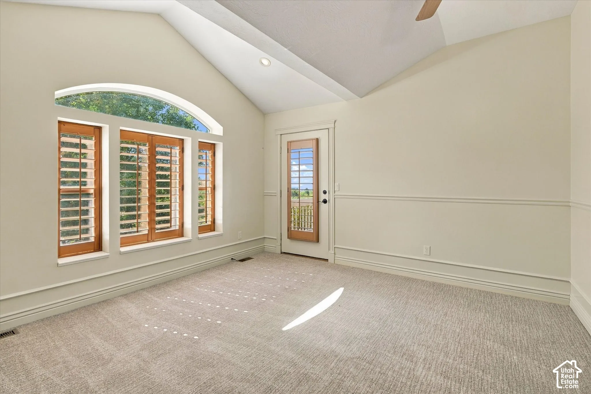 Vaulted ceiling, arched transom window, wood-frame windows with plantation shutters, wainscoting, and carpet flooring