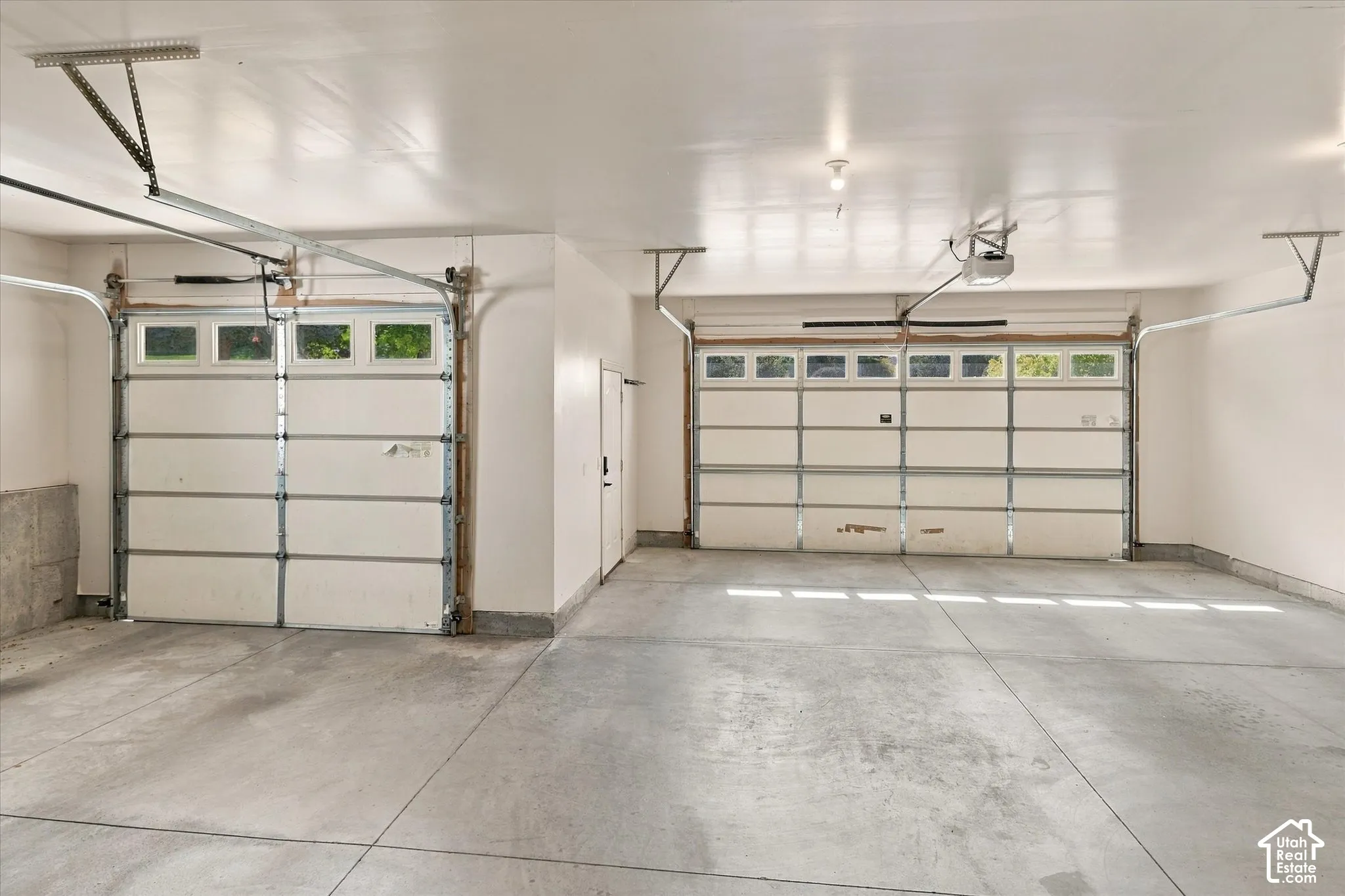 Two-car garage with concrete flooring, two overhead garage doors with window panels, and interior access door