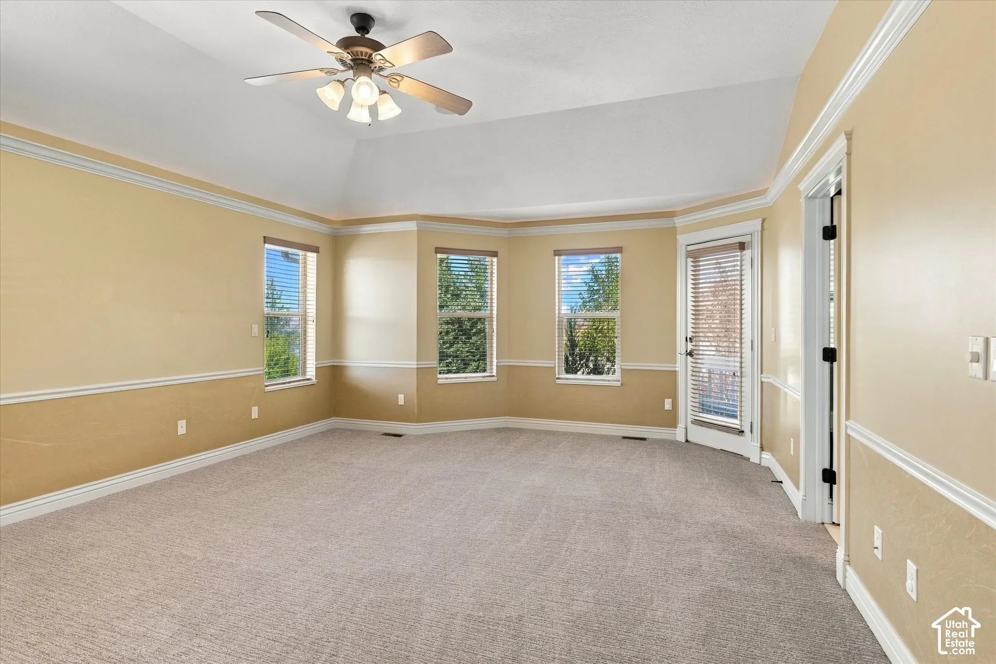 Vaulted ceiling with a ceiling fan, carpet flooring, multiple windows with blinds, and a glass-paneled door
