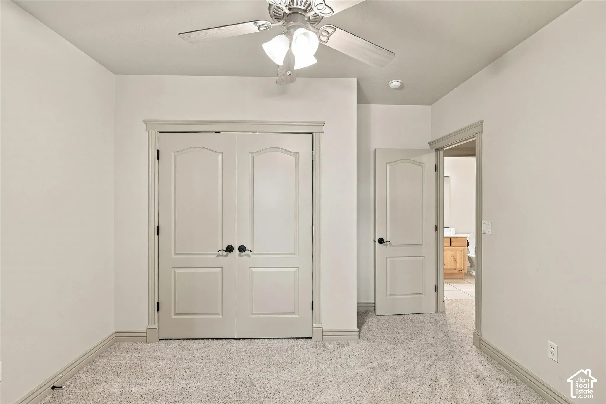 Textured carpeting, ceiling fan with light fixture, double panel doors, painted trim, and a single panel door