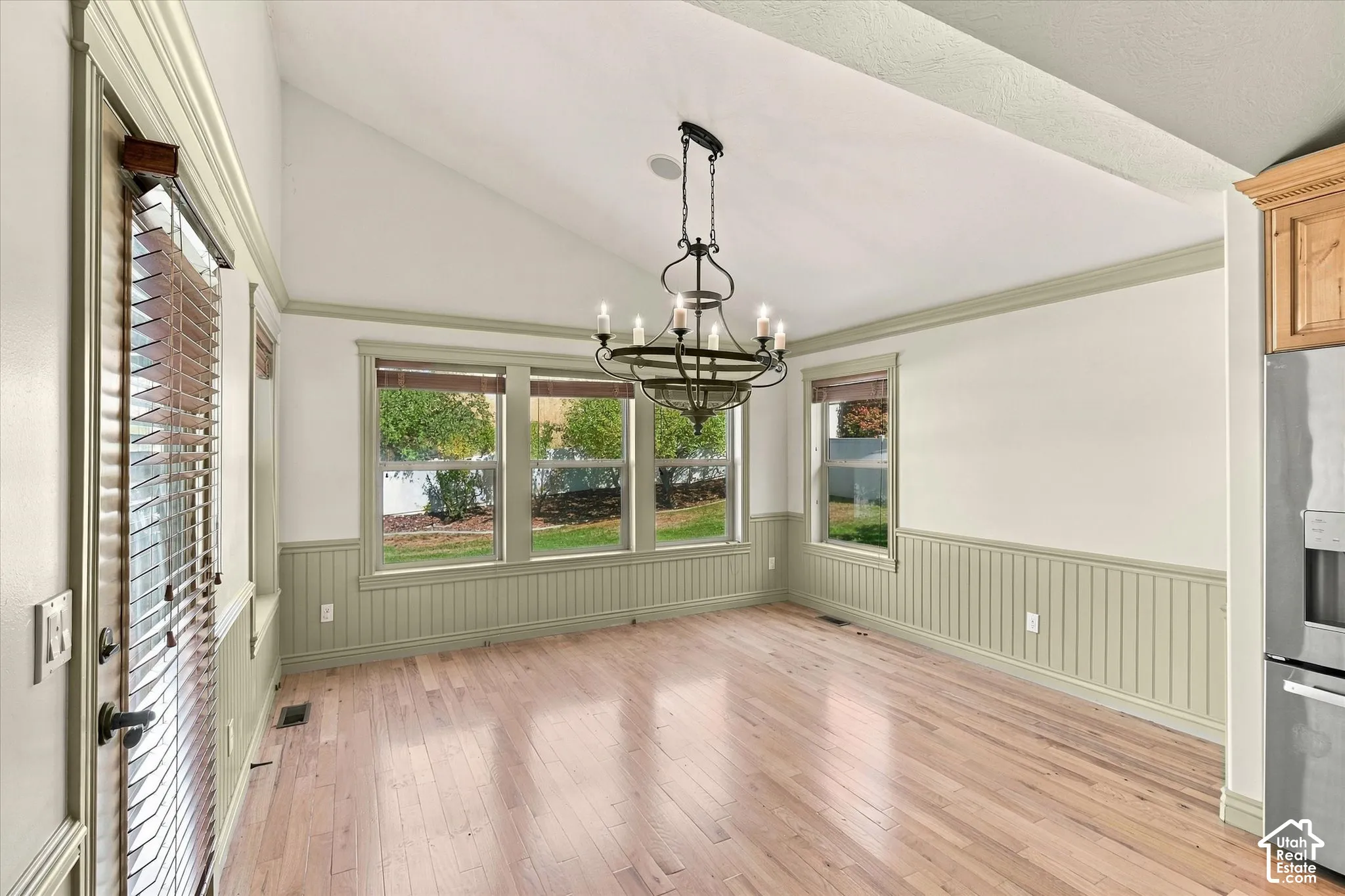 Wood-finish flooring, vaulted ceiling, beadboard wainscoting, multiple windows, and a chandelier