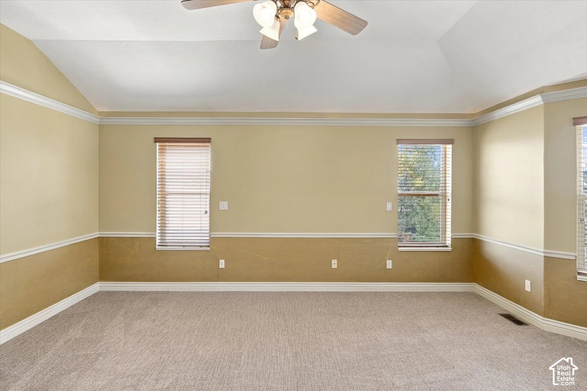 Vaulted ceiling with a ceiling fan, carpeted flooring, multiple windows, and two-tone wall treatment with crown molding