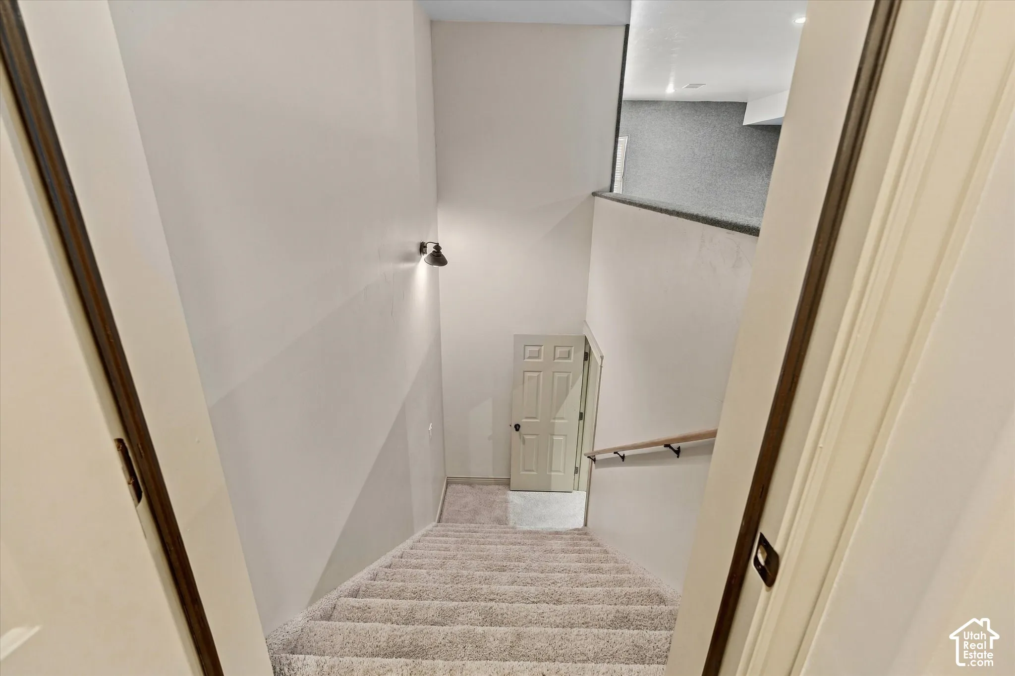 Carpeted staircase with a wood handrail, featuring a wall-mounted light fixture