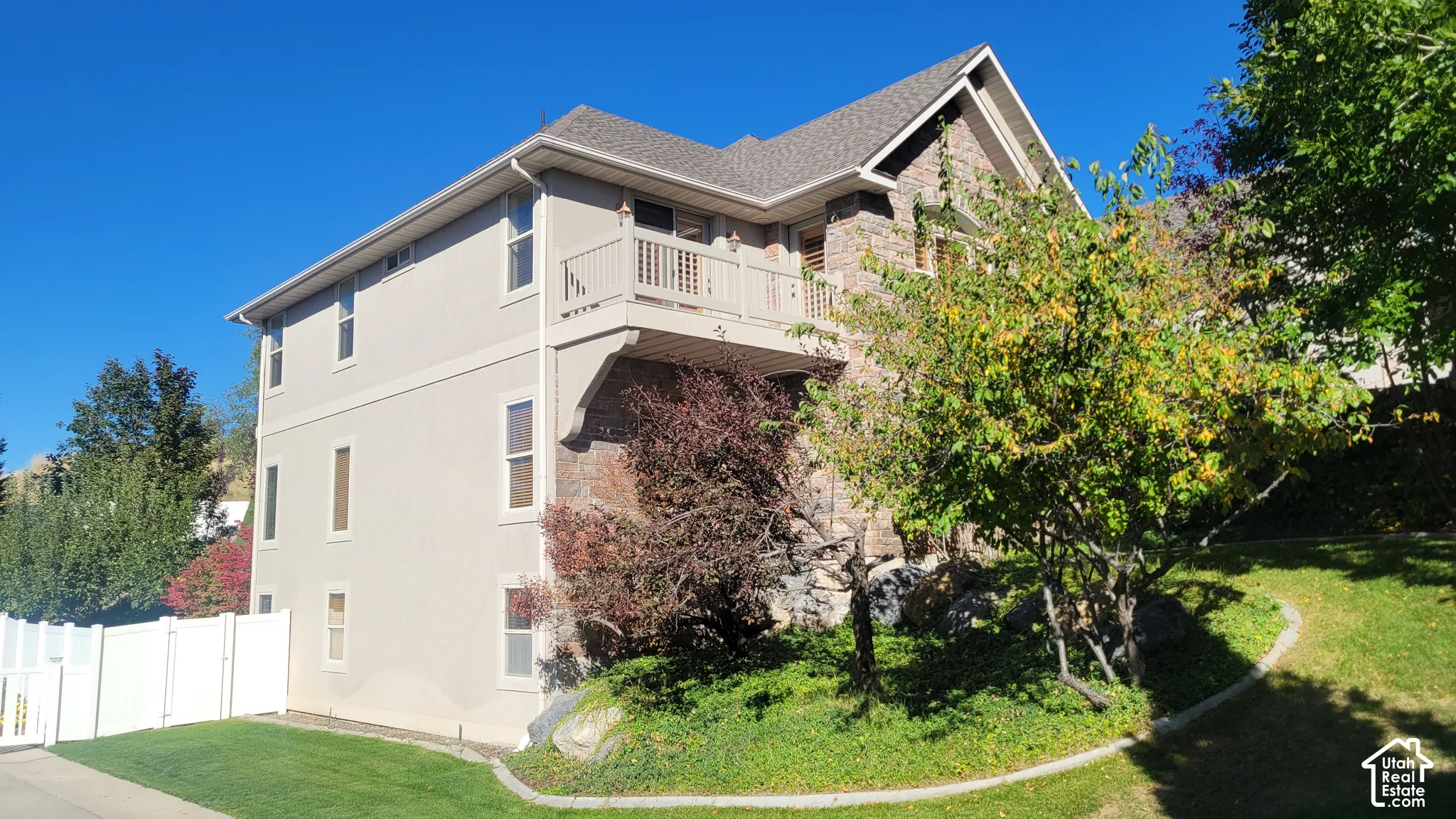 Multi-level exterior featuring stucco and stone facade, private balcony with railing, and a gabled roof