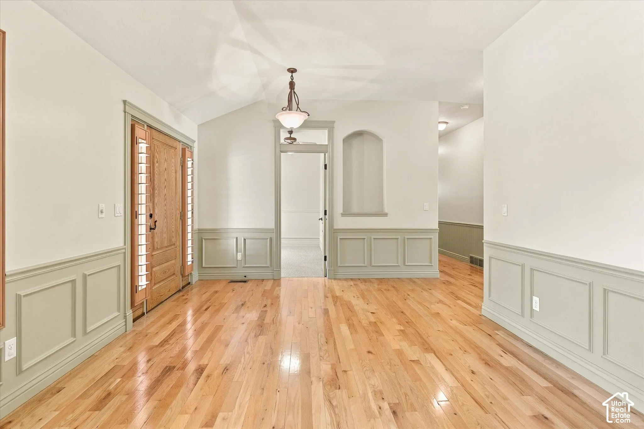 Hardwood flooring, wainscoting, vaulted ceiling, arched doorway, and built-in wall niche