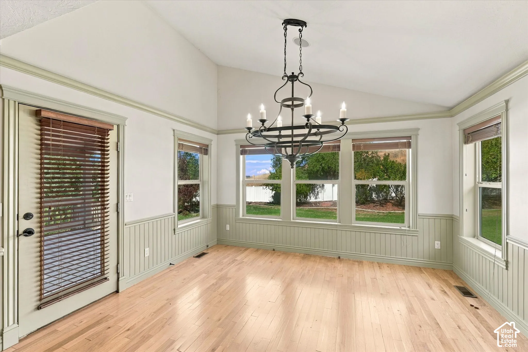 Vaulted ceiling, natural wood-finish flooring, wainscoting, multiple windows, and a large chandelier