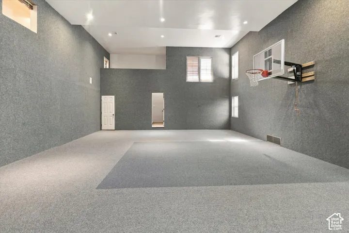 Expansive recreational space featuring two-tone carpeting, high ceilings with recessed lighting, and a mounted basketball hoop