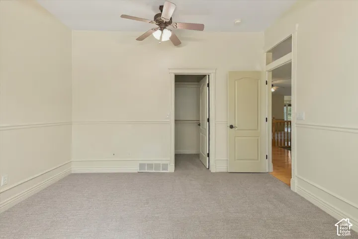 Neutral wall paint, wainscoting detail, ceiling fan with light fixture, paneled doors, and carpeted flooring
