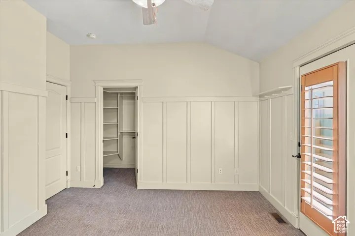 Vaulted ceiling, ceiling fan, board and batten wall treatment, carpeted flooring, walk-in closet with shelving