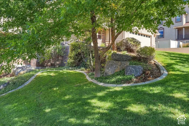 Landscaped yard with a manicured lawn, established trees, decorative boulders, and concrete curbing