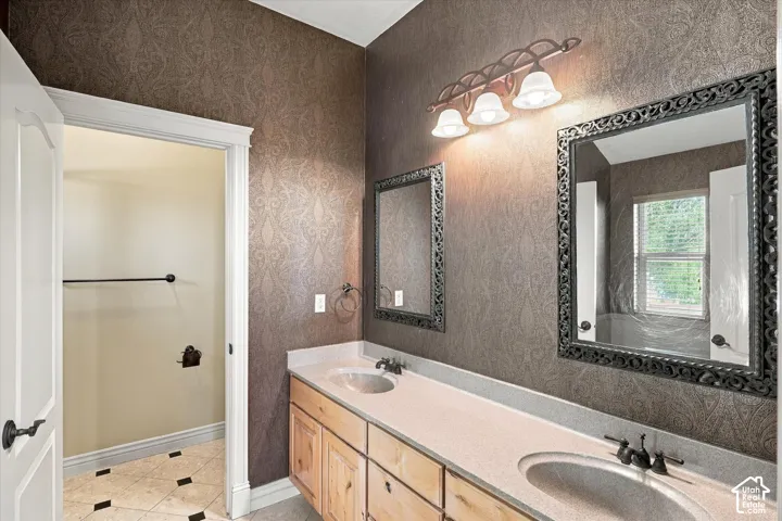Dual vanity with integrated sinks and dark bronze fixtures, light wood-finish cabinetry, decorative mirror frames, and patterned wallpaper
