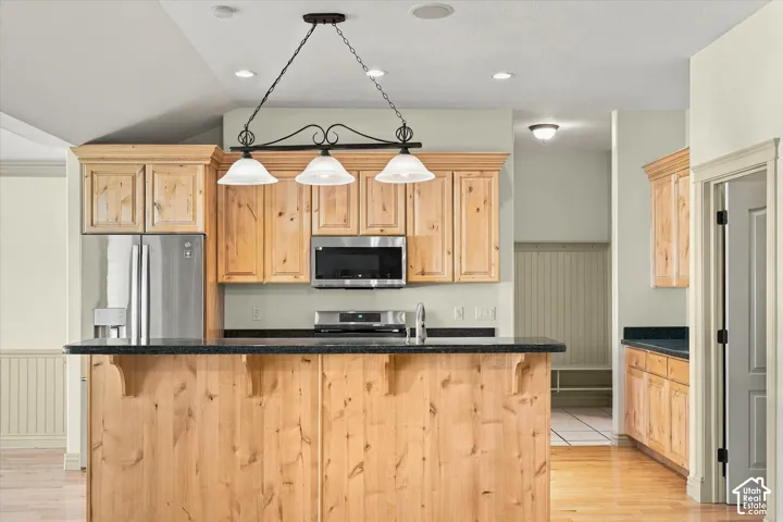 Natural wood cabinetry with crown molding, stainless steel appliances, dark stone countertops, wood-finish flooring, and recessed lighting