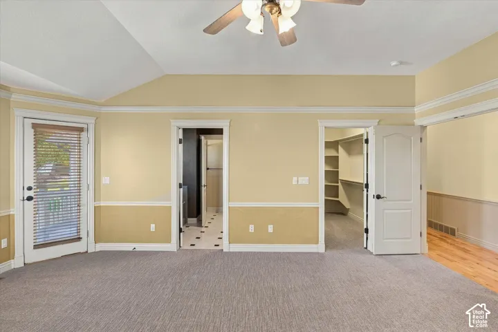 Vaulted ceiling with ceiling fan, carpet flooring, walk-out access, and built-in closet shelving
