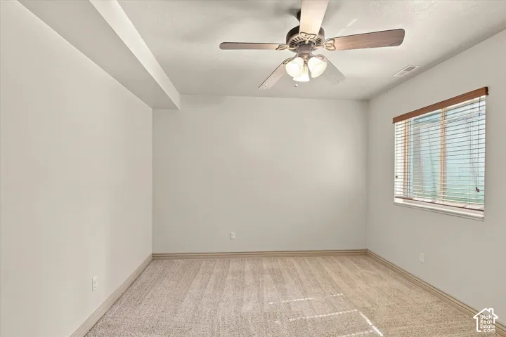 Recessed ceiling beam with flush lighting, ceiling fan with integrated lighting, window with wood-finish blinds, and neutral-toned carpet flooring