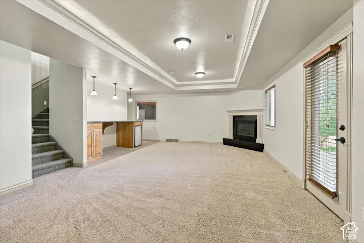 Recessed lighting, tray ceiling, built-in fireplace, wet bar with wood-finish cabinetry, and glass-paneled door