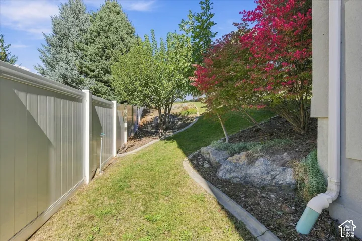 Landscaped side yard featuring a privacy fence, established green lawn, and mature trees
