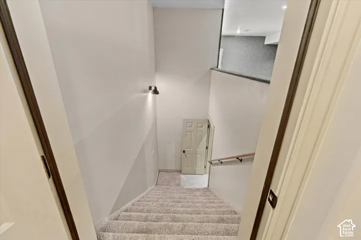 Carpeted staircase with a wood handrail, featuring a wall-mounted light fixture
