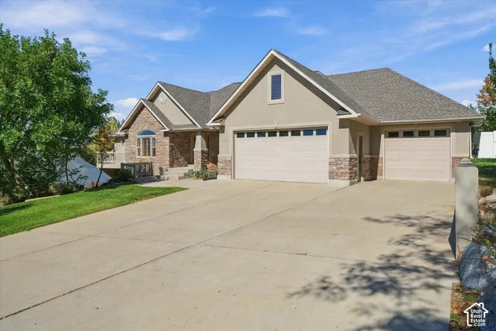 Stucco and stone exterior with architectural shingles, multiple garage doors, a concrete driveway, and a manicured lawn