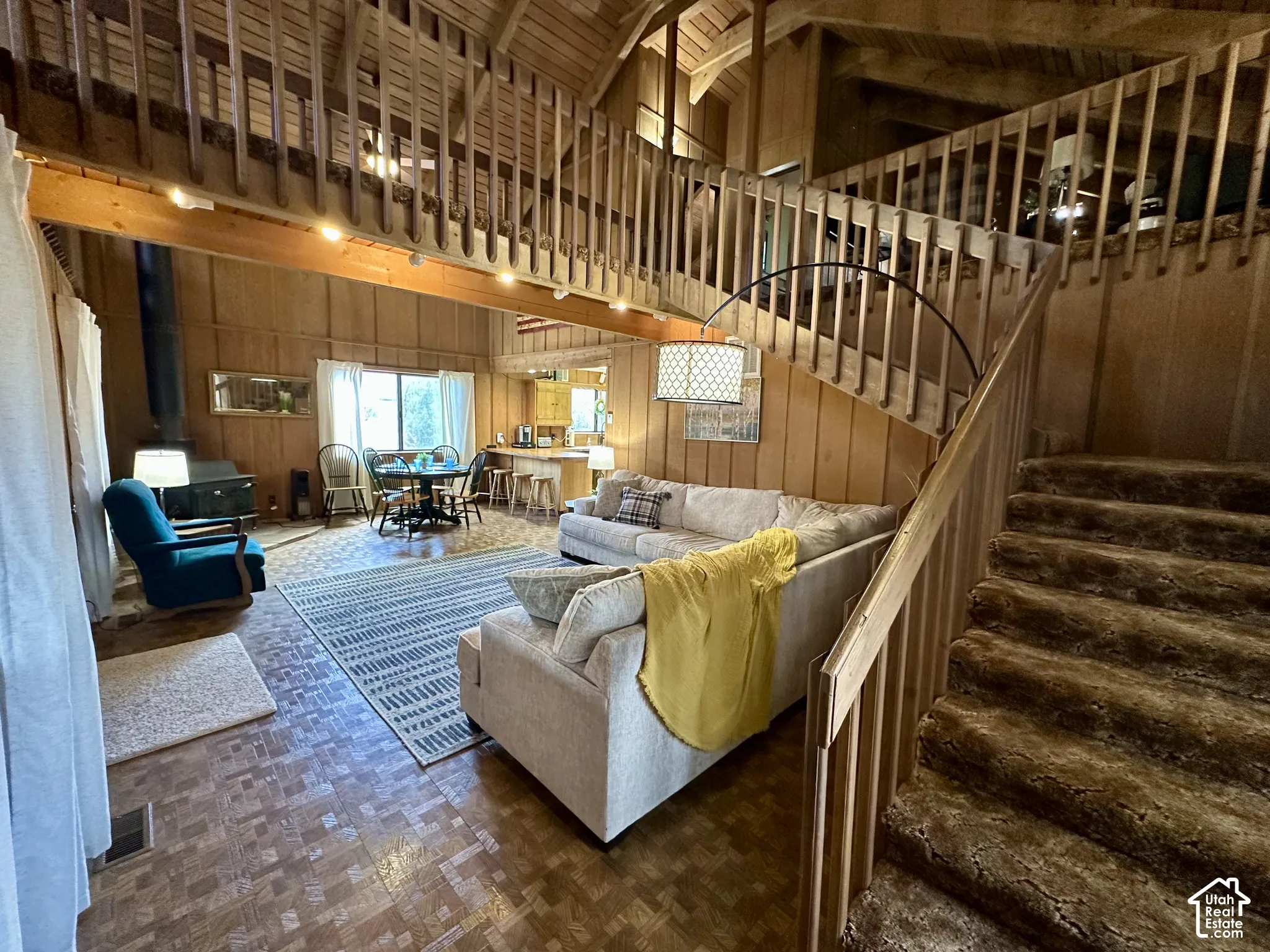 Wood paneling throughout, vaulted ceilings with exposed beams, wood-finish flooring, a wood-burning stove, and a full staircase with a second-story landing