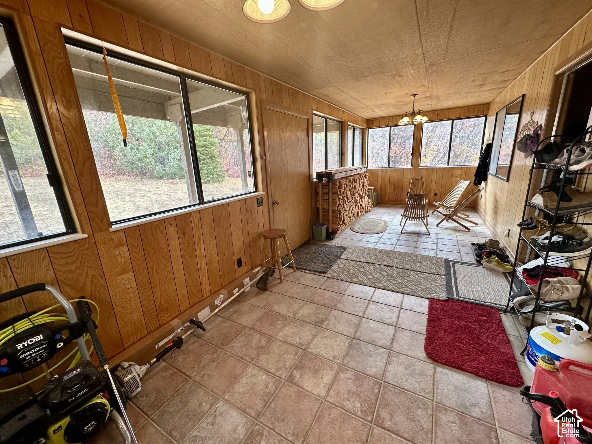 Enclosed sunroom featuring tile flooring, wood-paneled walls, multiple windows, and an overhead light fixture