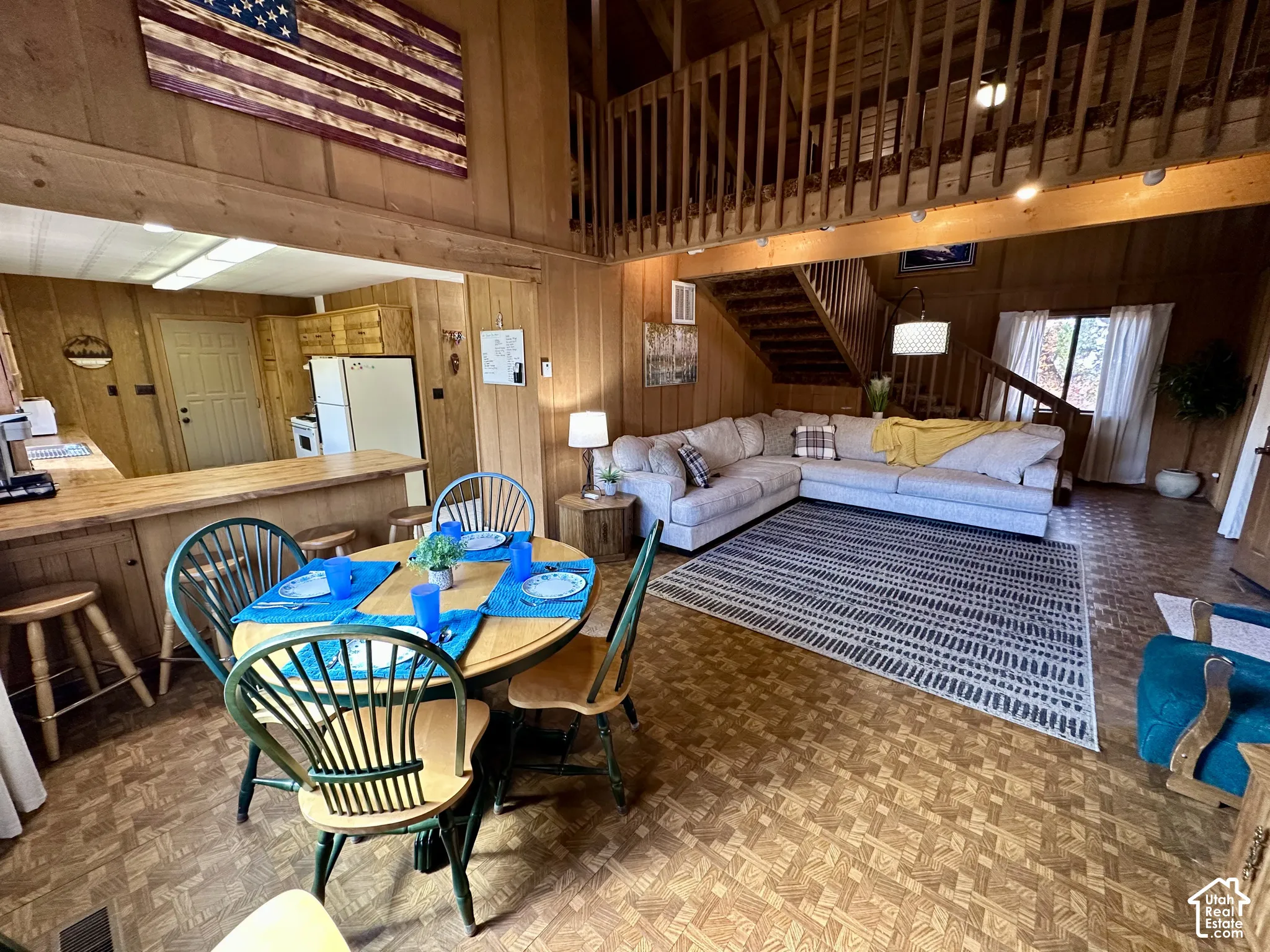 Open-concept living area with wood-paneled walls, exposed wood beams, and patterned wood-finish flooring
