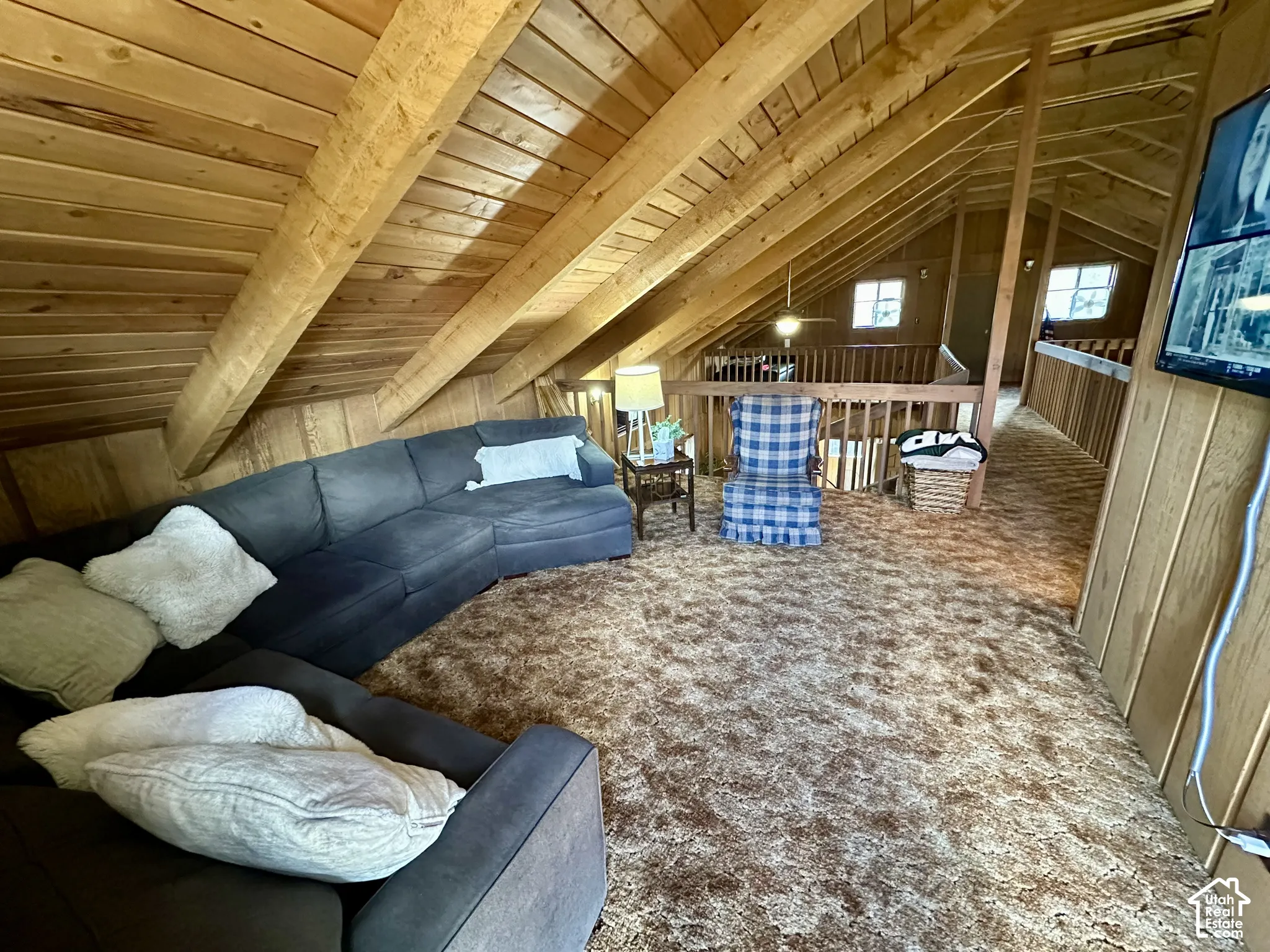 Vaulted ceiling with exposed wood beams, wood paneling, wood railing, and two windows