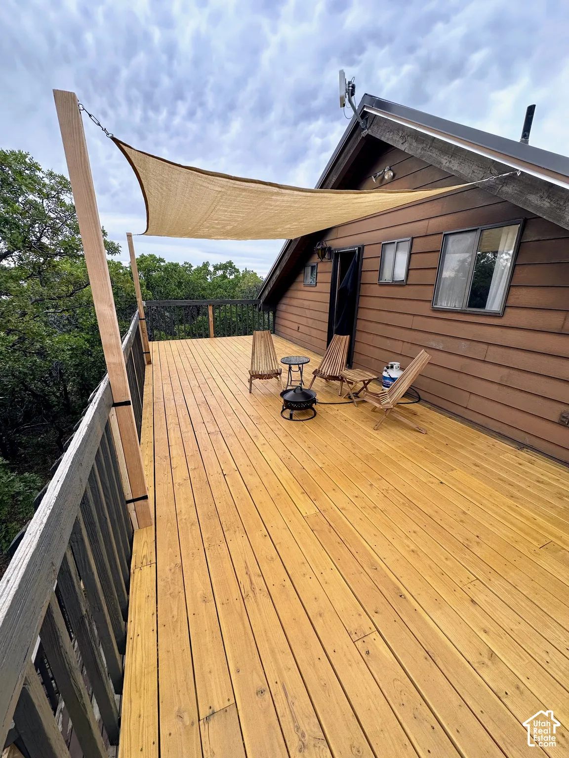 Expansive wood-plank deck with a partial shade awning, featuring a wood-sided exterior, a pitched roofline, and multiple windows