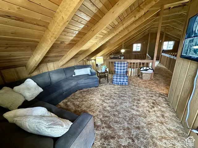 Vaulted ceiling with exposed wood beams, wood paneling, wood railing, and two windows