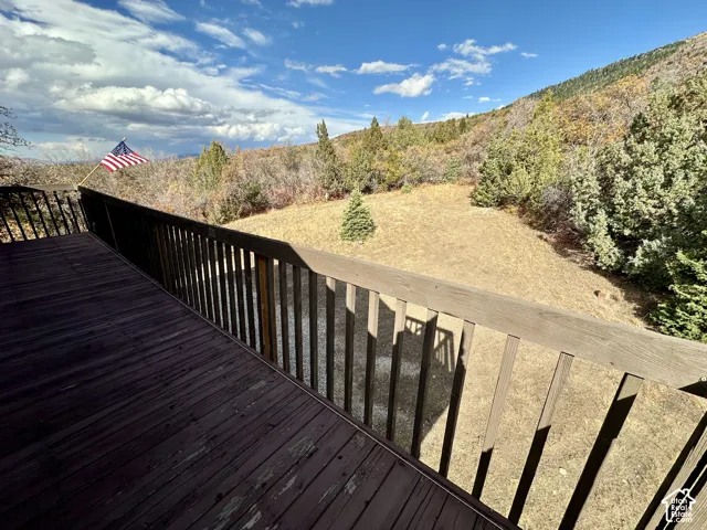 Expansive outdoor deck with wood railing, offering broad mountainous and vegetated terrain