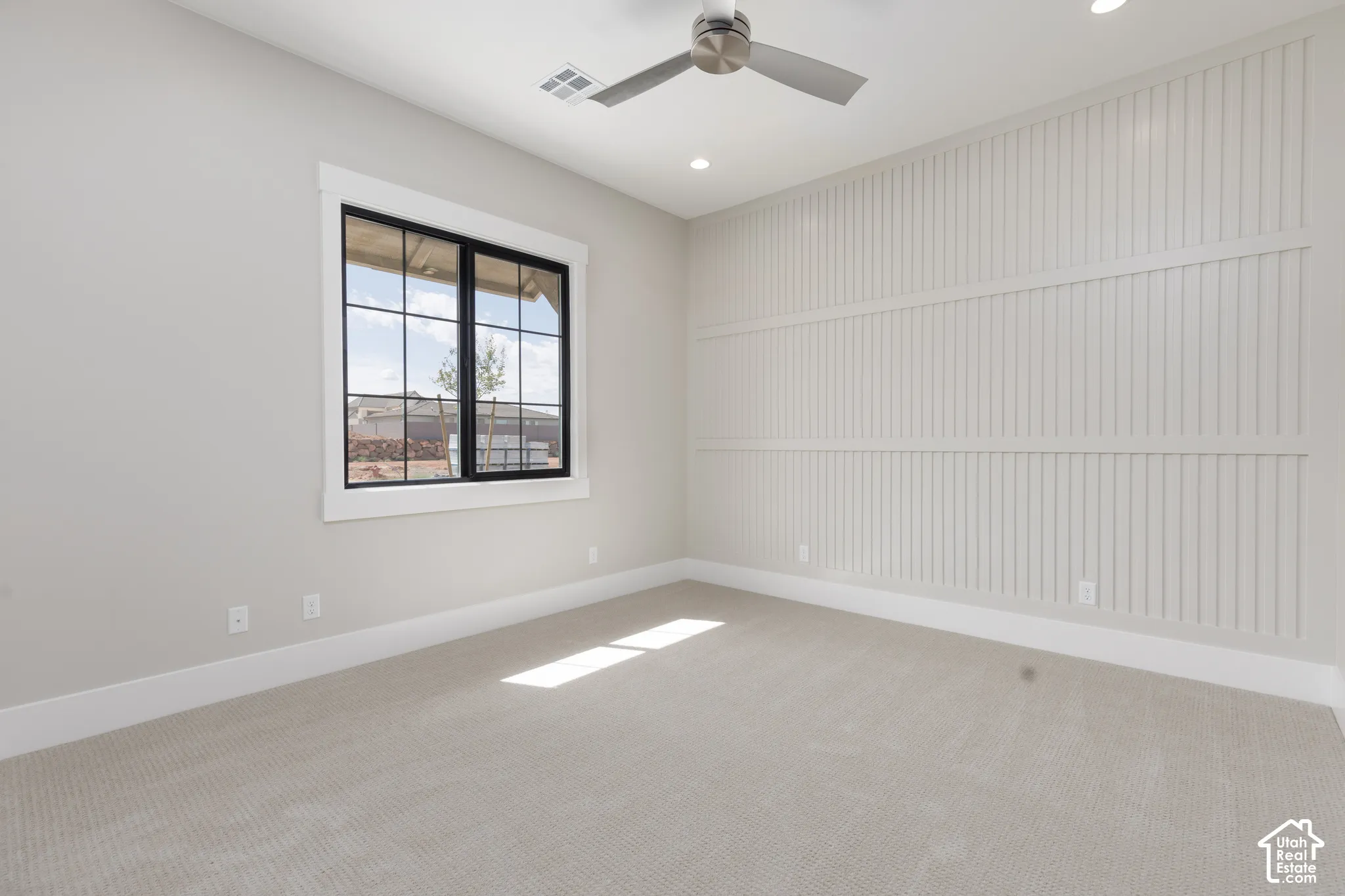 Textured accent wall, window with black framing, recessed lighting, ceiling fan, and light-toned carpeting