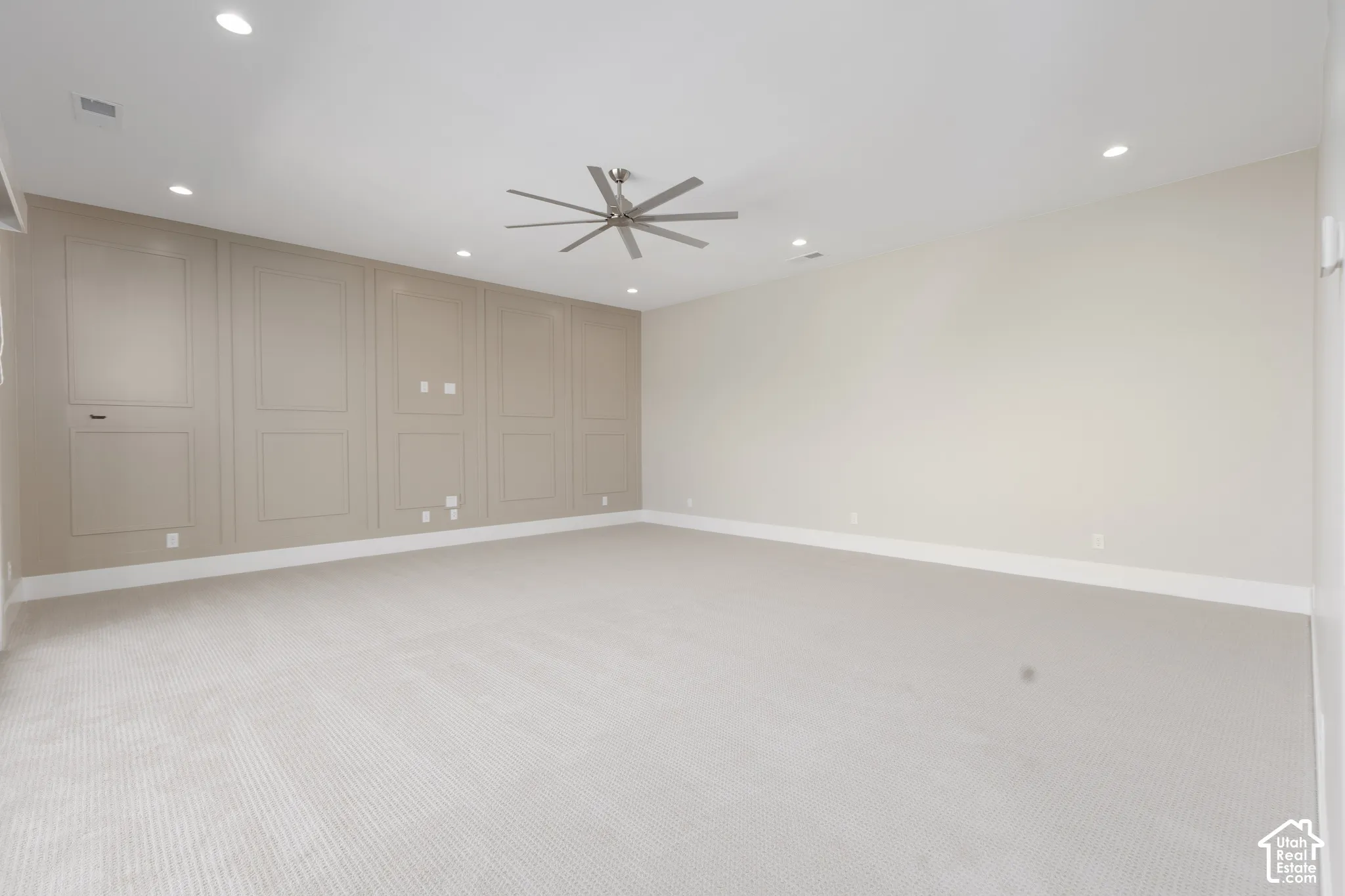Recessed lighting, ceiling fan, accent wall with panel molding, light-toned carpeting, and crisp white trim