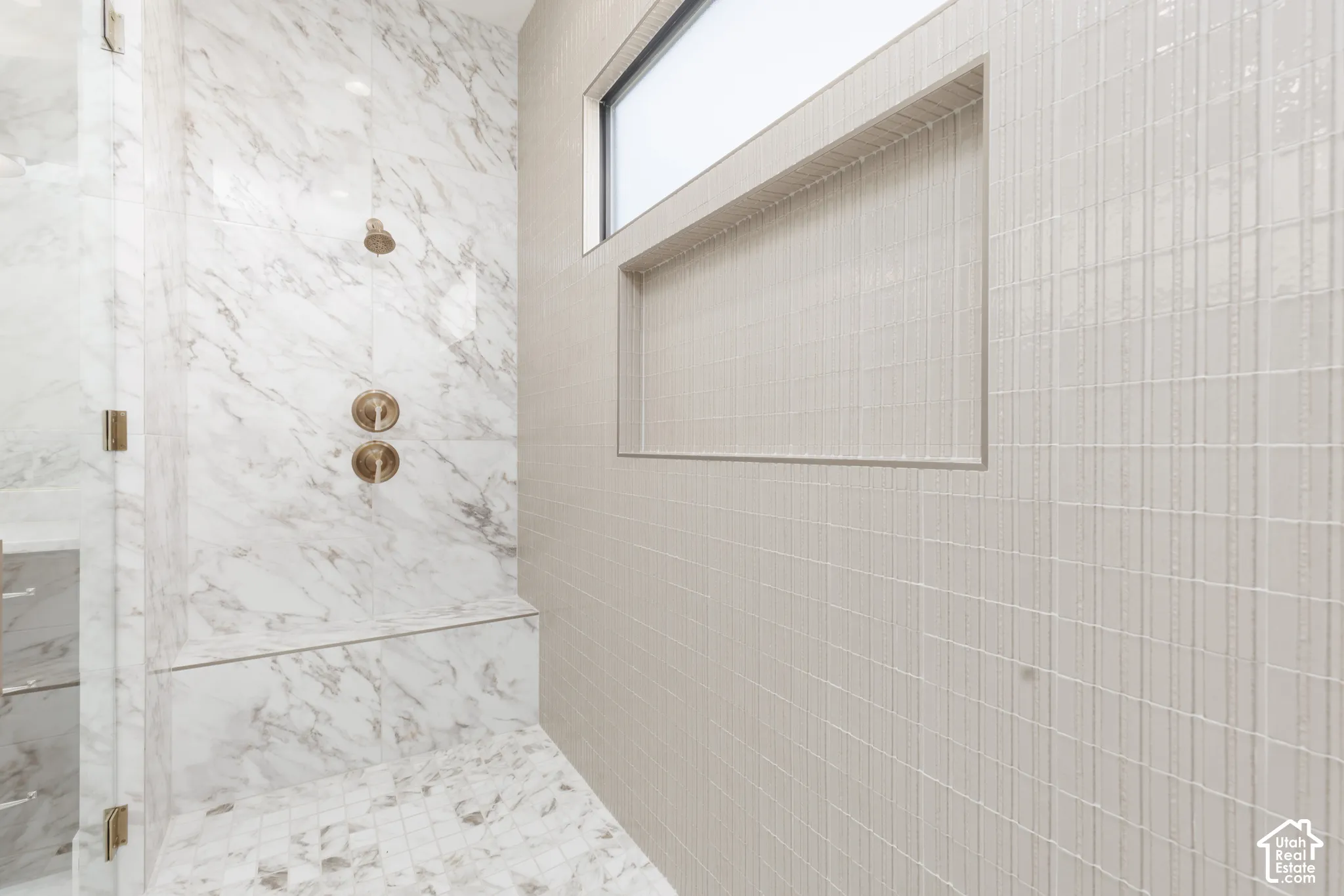 Walk-in shower with marble-finish tiling, integrated bench, and bronze-finish fixtures