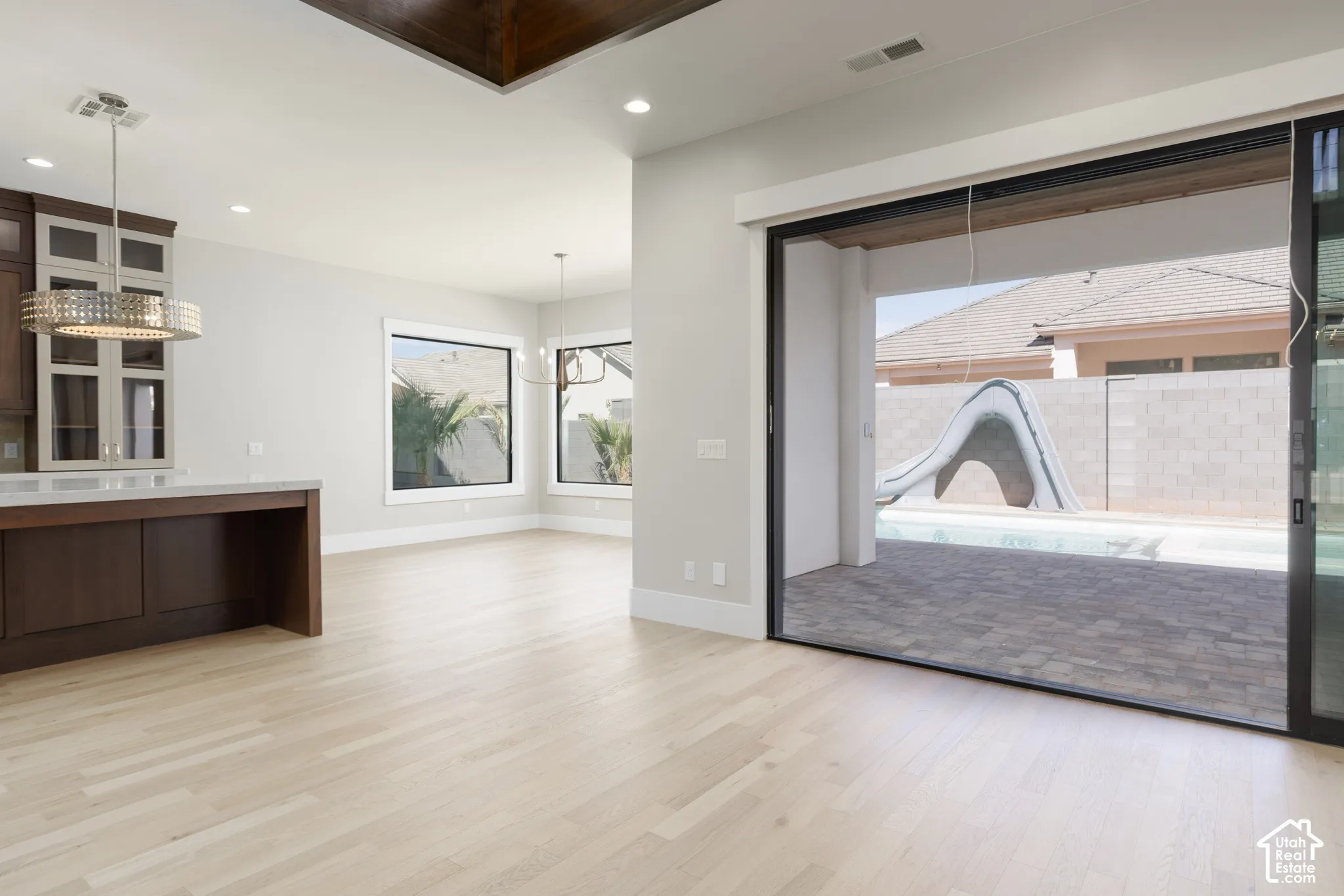 Wide plank wood-finish flooring, recessed lighting, and a modern chandelier illuminate the expansive living area