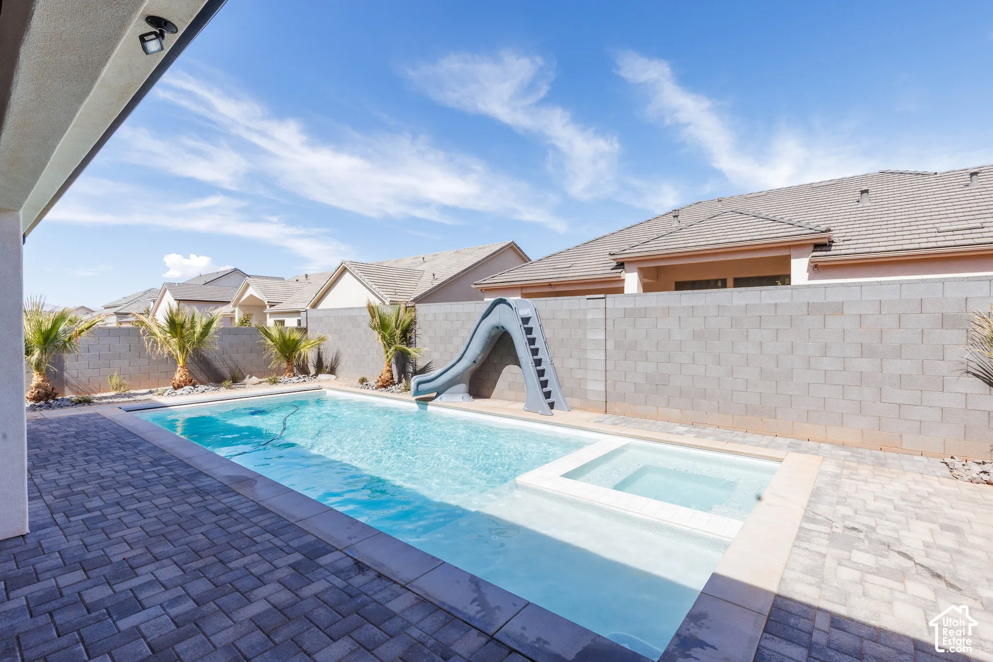 Outdoor swimming pool with an integrated spa, a built-in slide, and paver decking